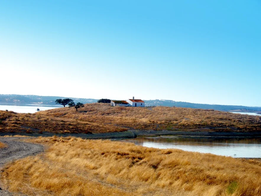 The Alqueva lake near Monsaraz in the Alentejo, golden grass and a whitewashed farmhouse on the hill
