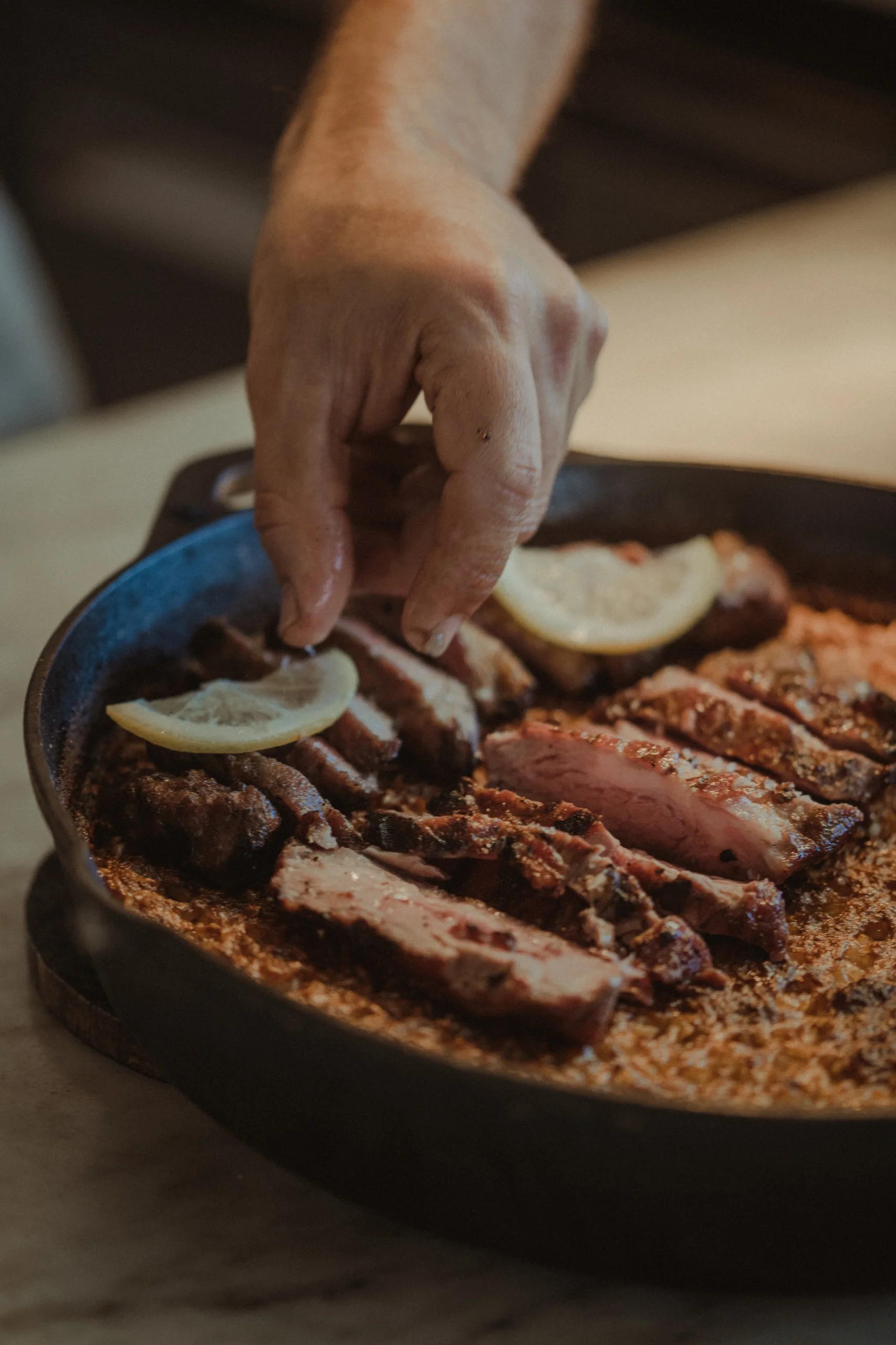 Grilled meat with slices of lemon, served in a cast-iron pan at the table